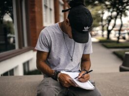 Best Creative Writing Graduate Programs in the World person in black adidas cap sitting on bench writing on notebook