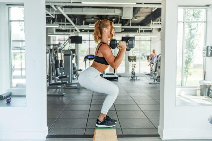 Photo by Benjamin Klaver woman wearing black sports bra and white legging lifting dummbells