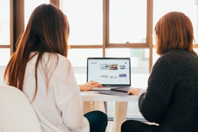 Photo by KOBU Agency two women talking while looking at laptop computer