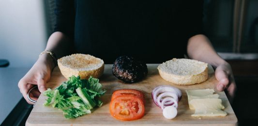 How Fast Food Chains Are Leveraging Online Marketing woman holding up wooden tray with lettuce, tomato, onions rings and cooked patty for burger