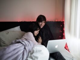 13 Most Inspiring Movies of All Time You Should Watch on Hulu couple on bed using MacBook Air beside of window with white curtain