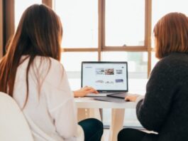 Importance of Online Proctoring in Remote Hiring two women talking while looking at laptop computer