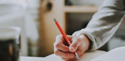 Different Types of Academic Writing person holding on red pen while writing on book