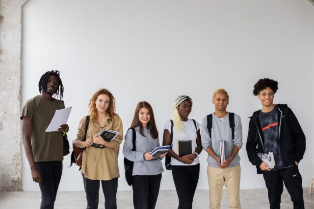 Photo by Monstera Production Group of diverse young multiracial classmates with notebooks and textbooks and backpacks smiling at camera