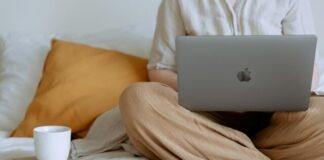 The Rise of Online Casino Entertainment in Singapore: A Tale of Digital Euphoria Crop faceless female in casual outfit sitting on bed with legs crossed holding laptop on knees with cup of coffee standing on notebook while working from home