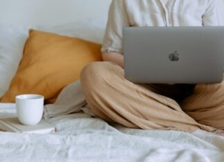 The Rise of Online Casino Entertainment in Singapore: A Tale of Digital Euphoria Crop faceless female in casual outfit sitting on bed with legs crossed holding laptop on knees with cup of coffee standing on notebook while working from home