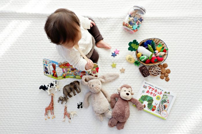 Photo by Yuri Shirota boy sitting on white cloth surrounded by toys