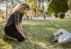 What Is The Difference Between A Survival Action And A Wrongful Death Claim? A woman kneeling by a grave in a sunlit cemetery, expressing grief and remembrance.