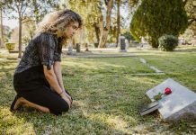 What Is The Difference Between A Survival Action And A Wrongful Death Claim? A woman kneeling by a grave in a sunlit cemetery, expressing grief and remembrance.