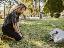 What Is The Difference Between A Survival Action And A Wrongful Death Claim? A woman kneeling by a grave in a sunlit cemetery, expressing grief and remembrance.