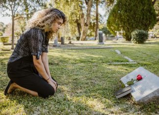 What Is The Difference Between A Survival Action And A Wrongful Death Claim? A woman kneeling by a grave in a sunlit cemetery, expressing grief and remembrance.