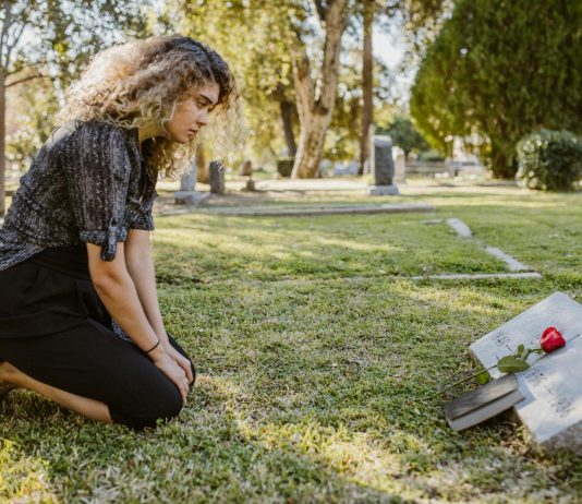 What Is The Difference Between A Survival Action And A Wrongful Death Claim? A woman kneeling by a grave in a sunlit cemetery, expressing grief and remembrance.