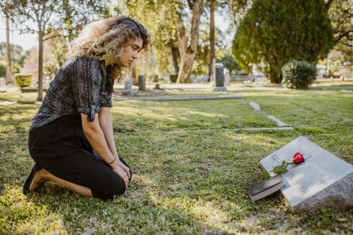 Photo by RDNE Stock project A woman kneeling by a grave in a sunlit cemetery, expressing grief and remembrance.