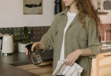 The Hidden Germ Zones in Your Home You’re Probably Ignoring A woman with curly hair cleans a kitchen counter using a spray bottle and cloth.