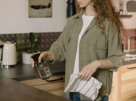 The Hidden Germ Zones in Your Home You’re Probably Ignoring A woman with curly hair cleans a kitchen counter using a spray bottle and cloth.