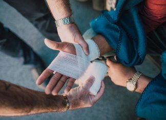 Understanding Comparative Fault In Florida Personal Injury Cases Close-up of two people bandaging an injured hand outdoors, focusing on first aid care.