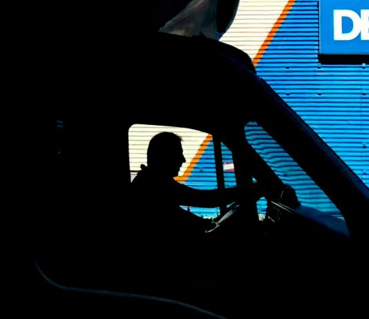 Can You Sue a Trucking Company for Driver Error? Silhouette of a driver in a vehicle with a blue industrial backdrop, illustrating transportation.