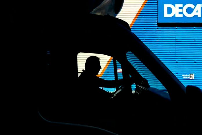 Photo by Kagan Bastimar Silhouette of a driver in a vehicle with a blue industrial backdrop, illustrating transportation.