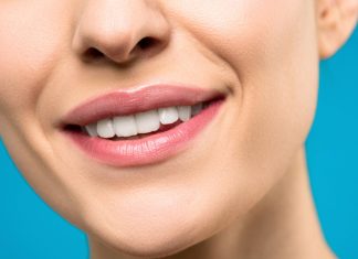 The Morning Habit That’s Quietly Damaging Your Teeth A close-up image of a woman's smile with pink lipstick and white teeth against a blue background.