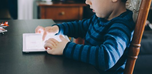 Struggling to Limit Your Child’s Screen Time? Try This Instead boy sitting on chair beside table using tablet computer