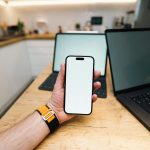 Top Reasons Businesses are Switching to an Alternative to Guardsquare A hand holds a phone with two laptops behind it.
