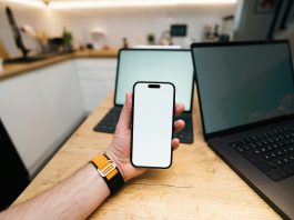 Top Reasons Businesses are Switching to an Alternative to Guardsquare A hand holds a phone with two laptops behind it.