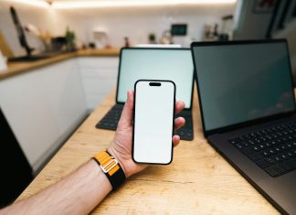 Top Reasons Businesses are Switching to an Alternative to Guardsquare A hand holds a phone with two laptops behind it.
