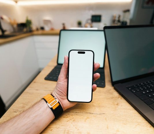 Top Reasons Businesses are Switching to an Alternative to Guardsquare A hand holds a phone with two laptops behind it.