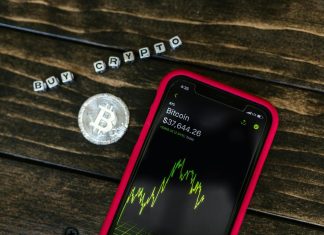 You Should Know About 5 Changes in Crypto Regulations Smartphone showing bitcoin price with a physical coin and text representing cryptocurrency investment.