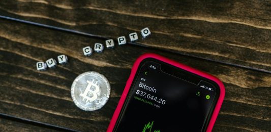 You Should Know About 5 Changes in Crypto Regulations Smartphone showing bitcoin price with a physical coin and text representing cryptocurrency investment.