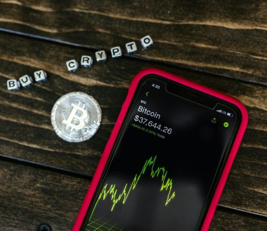 You Should Know About 5 Changes in Crypto Regulations Smartphone showing bitcoin price with a physical coin and text representing cryptocurrency investment.