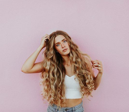 How Blonde Tape-In Hair Extensions Can Transform Your Look Instantly woman standing next to pink wall while scratching her head