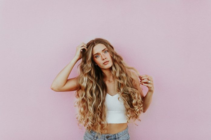 Photo by averie woodard woman standing next to pink wall while scratching her head