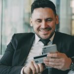 The Shift Toward Automated Financial Documentation in Modern Businesses Man in suit smiling while holding phone and credit card