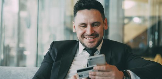 The Shift Toward Automated Financial Documentation in Modern Businesses Man in suit smiling while holding phone and credit card