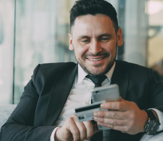 The Shift Toward Automated Financial Documentation in Modern Businesses Man in suit smiling while holding phone and credit card