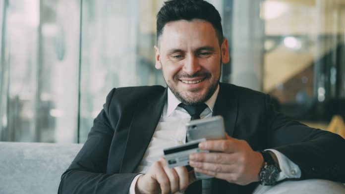 Photo by Vitaly Gariev Man in suit smiling while holding phone and credit card